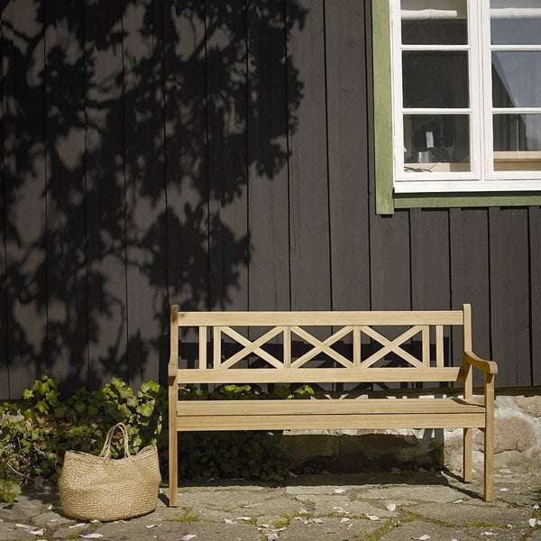 Light wood bench with cross pattern against a dark wood wall, complemented by a natural woven basket.