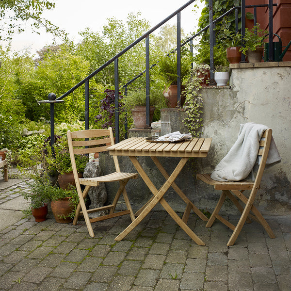 Light wood folding table and chairs set against a natural green landscape, featuring subtle earth tones and textured stone.