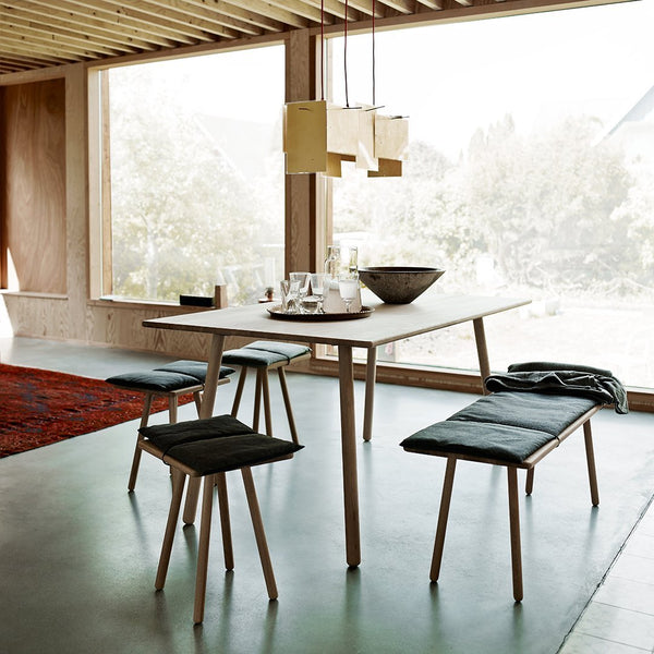 Modern dining table set featuring light wood, sleek black cushions, and vibrant red patterned rug in a bright, airy space.