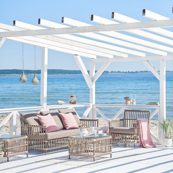 Chic outdoor seating in muted pink and beige, with a white frame and coastal views for a serene vibe.