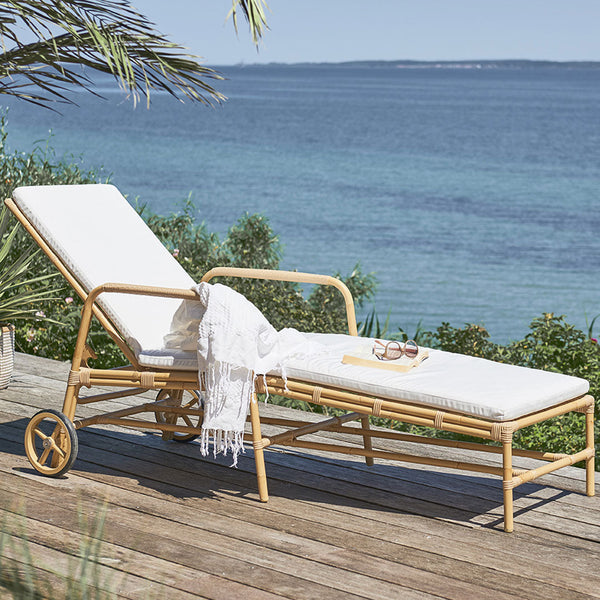 White cushioned lounge chair with natural rattan frame, set against a serene blue ocean backdrop. 