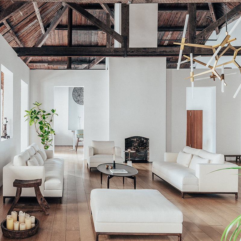 Modern white sofa set with wooden accents in a bright, open space featuring natural plants and wood floors.