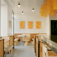 Modern cafe interior with warm orange and yellow accents, geometric wall art, and light wood furniture.