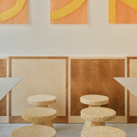Yellow and white speckled stools against warm orange and brown wall art, featuring bold geometric patterns.