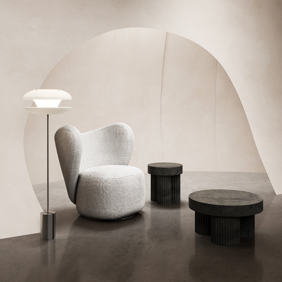Soft gray upholstered chair with smooth curves, paired with black accent tables in a minimalist, neutral-toned setting.