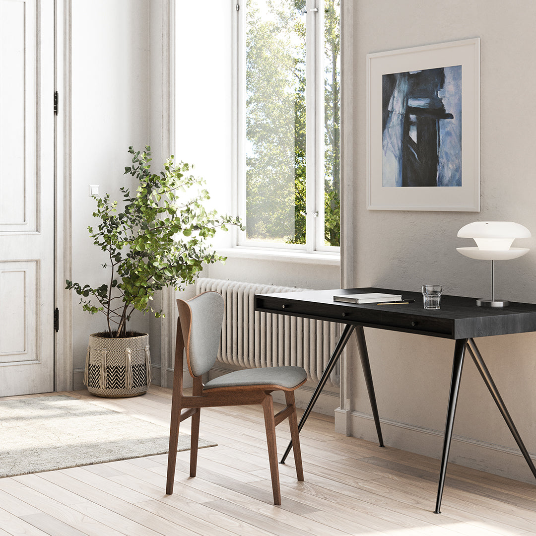 Modern black desk with wood legs, grey chair, and neutral tones. Lush greenery complements the minimalistic decor.