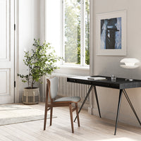 Modern black desk with wood legs, grey chair, and neutral tones. Lush greenery complements the minimalistic decor.