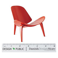 Red modern chair with smooth curves and a sleek design, set against a ruler for scale.