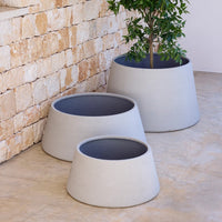 "Set of three tapered gray planters with smooth texture and contrasting dark interiors against a natural stone backdrop."