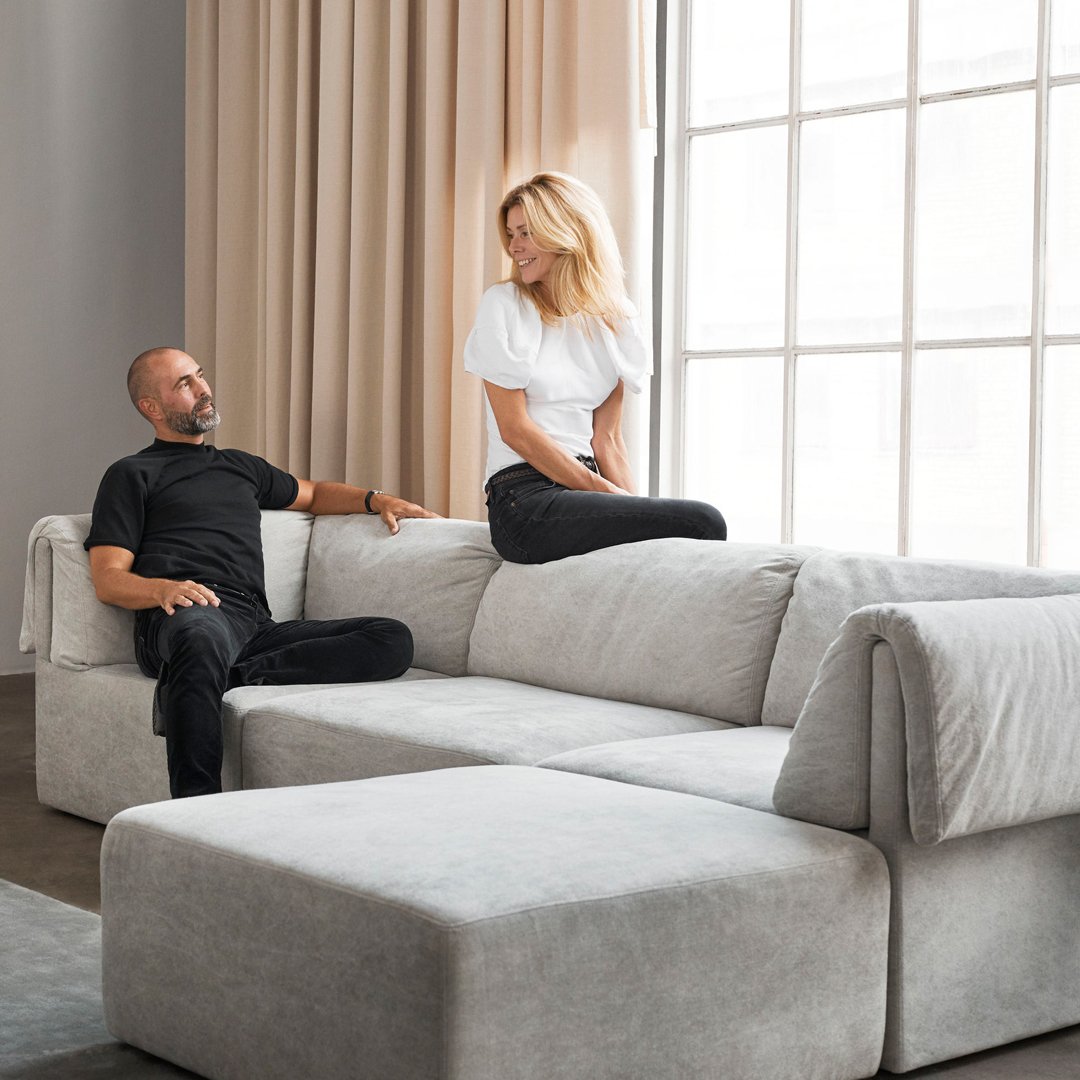 "Light gray sectional sofa with smooth fabric and minimalist design, set against neutral-toned curtains and contemporary decor."