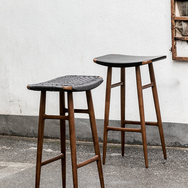 Two wooden bar stools with dark woven seats and sleek walnut legs, showcasing a modern, minimalist design.