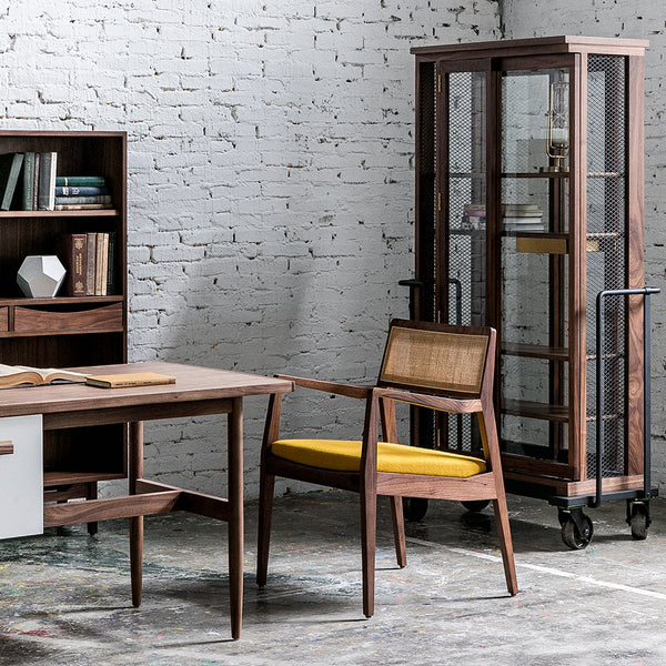 "Modern wooden desk with sleek lines, paired with a rattan chair featuring a pop of yellow, and a glass display cabinet."