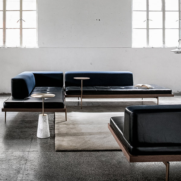 Modern black leather sofa with navy blue cushions and minimalist wood accents on a textured gray floor.