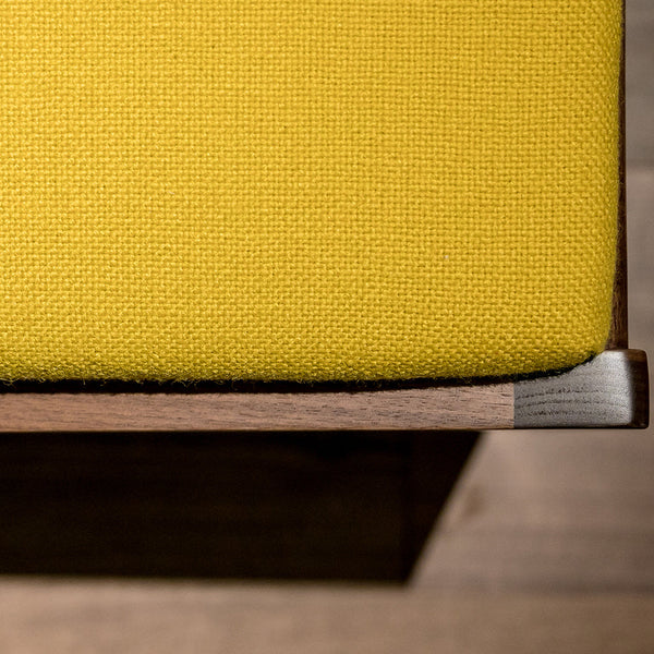 Yellow textured fabric cushion on a wooden stool, highlighting a vibrant color contrast and elegant design.