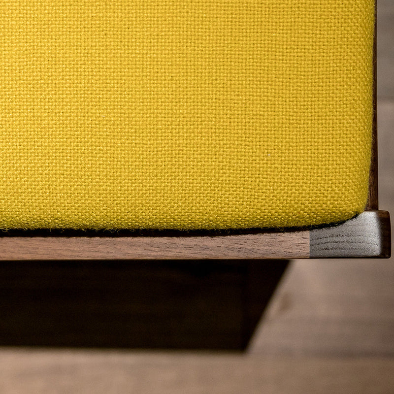 Yellow textured fabric cushion on a wooden stool, highlighting a vibrant color contrast and elegant design.