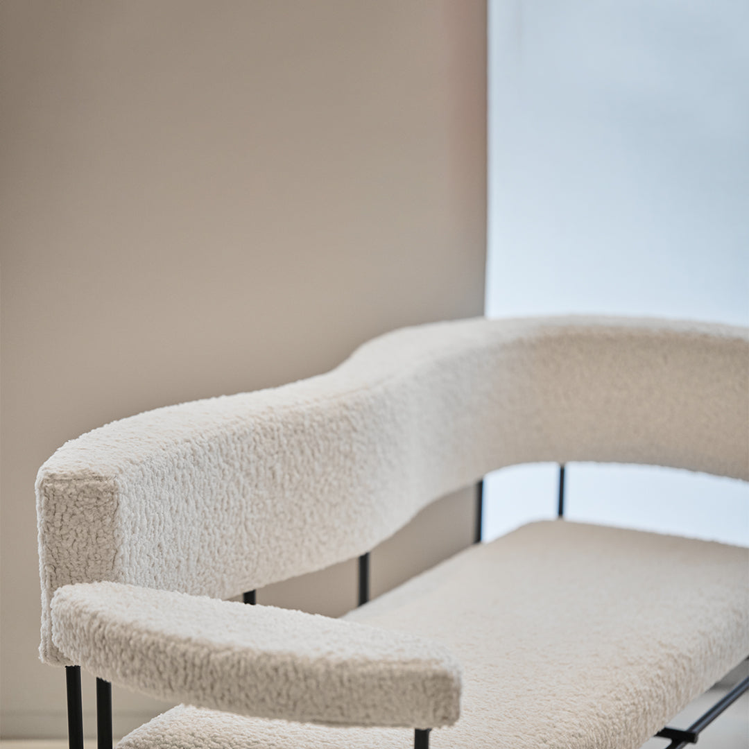 Curved white boucle chair with soft texture and sleek black frame against a minimalistic background.