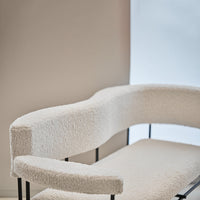 Curved white boucle chair with soft texture and sleek black frame against a minimalistic background.