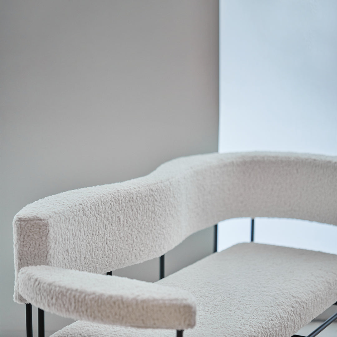 White curved sofa with a textured, fluffy finish, set against a minimalist light gray background.