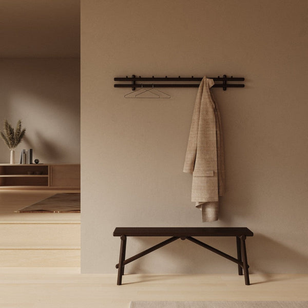 Neutral beige wall with a textured beige coat hanging on a black minimalist rack above a dark wooden bench.