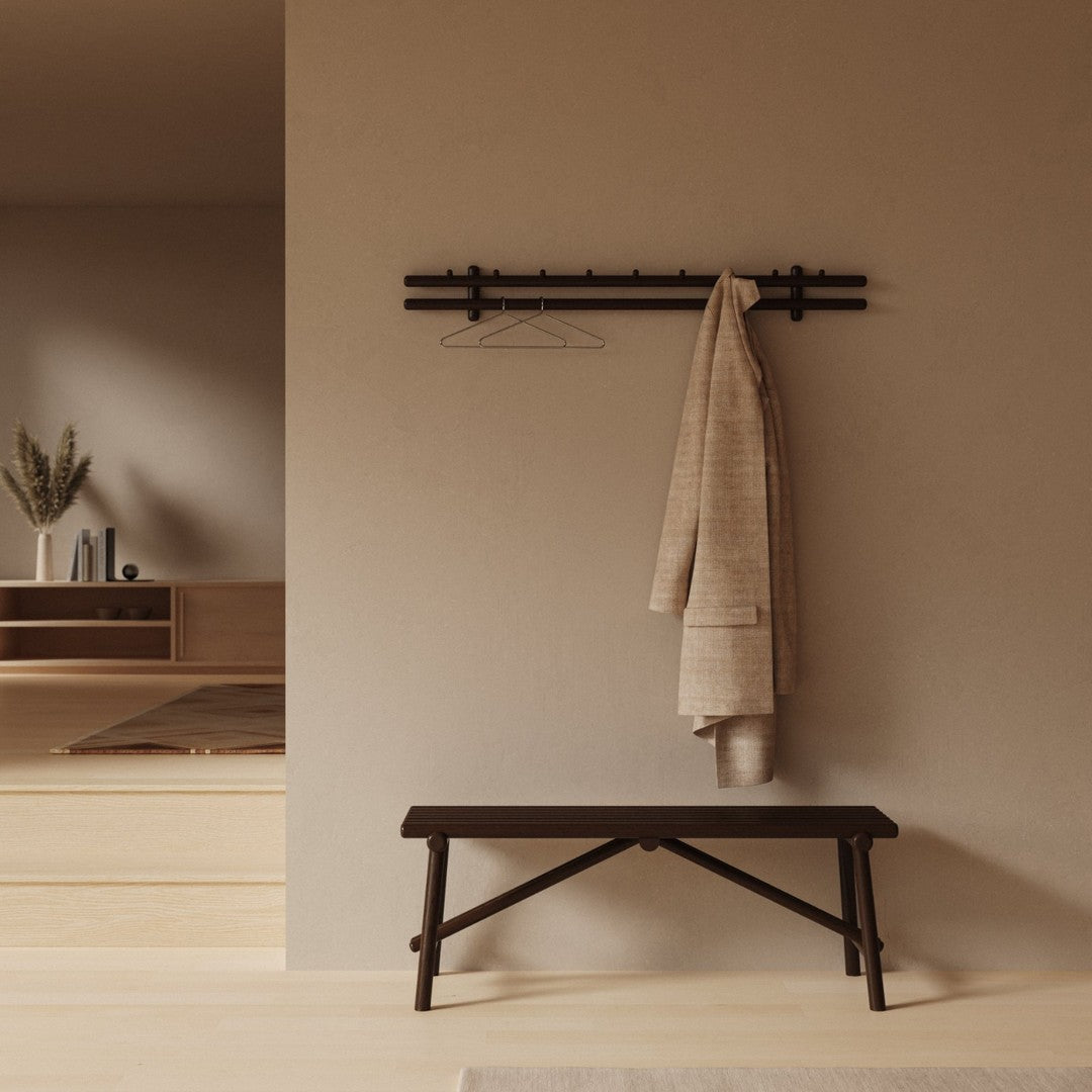 Neutral beige wall with a dark wooden coat rack and a black bench, featuring a textured cream coat hung on the rack.