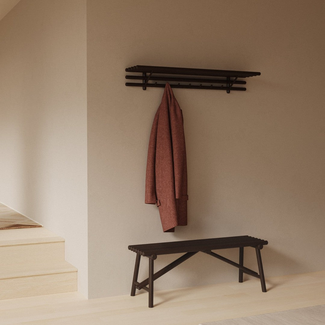 Dark wood bench and wall shelf with a deep red coat, against a light neutral wall. Minimalist design with earthy tones.