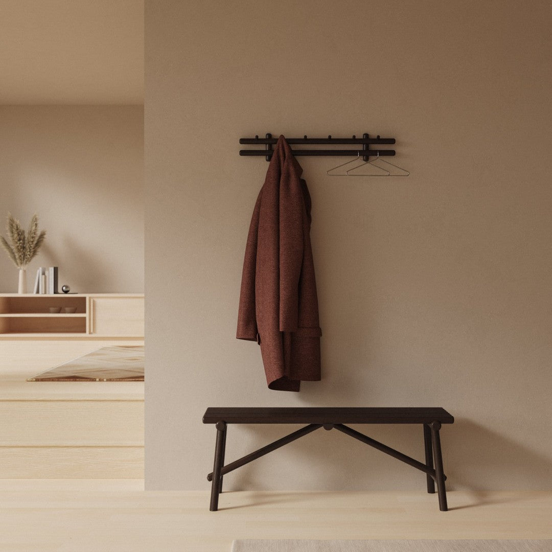 Rustic black bench with a warm, earthy-toned brown coat against a neutral beige wall. Minimalist design.