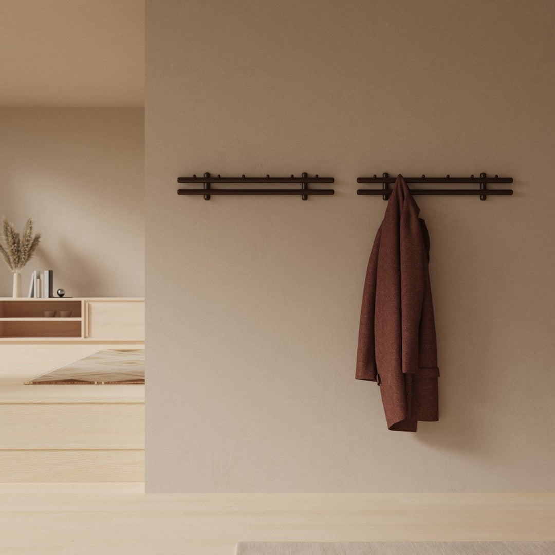Brown coat hanging on dark wood hooks against a warm beige wall, featuring minimalist design and earthy tones.