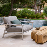 Grey textured outdoor armchair with white frame, paired with a wooden accent table and soft green pillow.