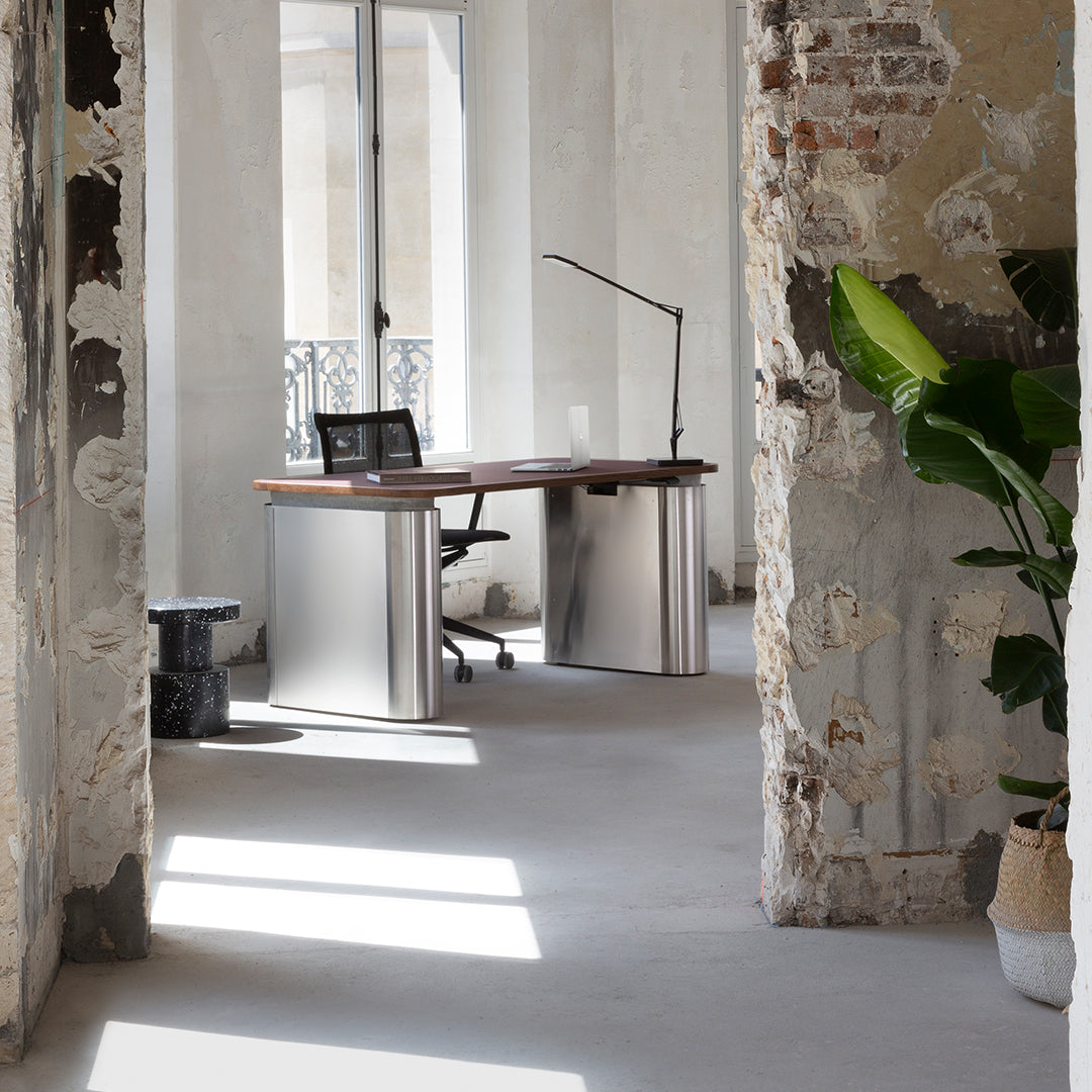 Modern desk with a natural wood finish and sleek silver accents, set against a backdrop of rustic, textured walls.