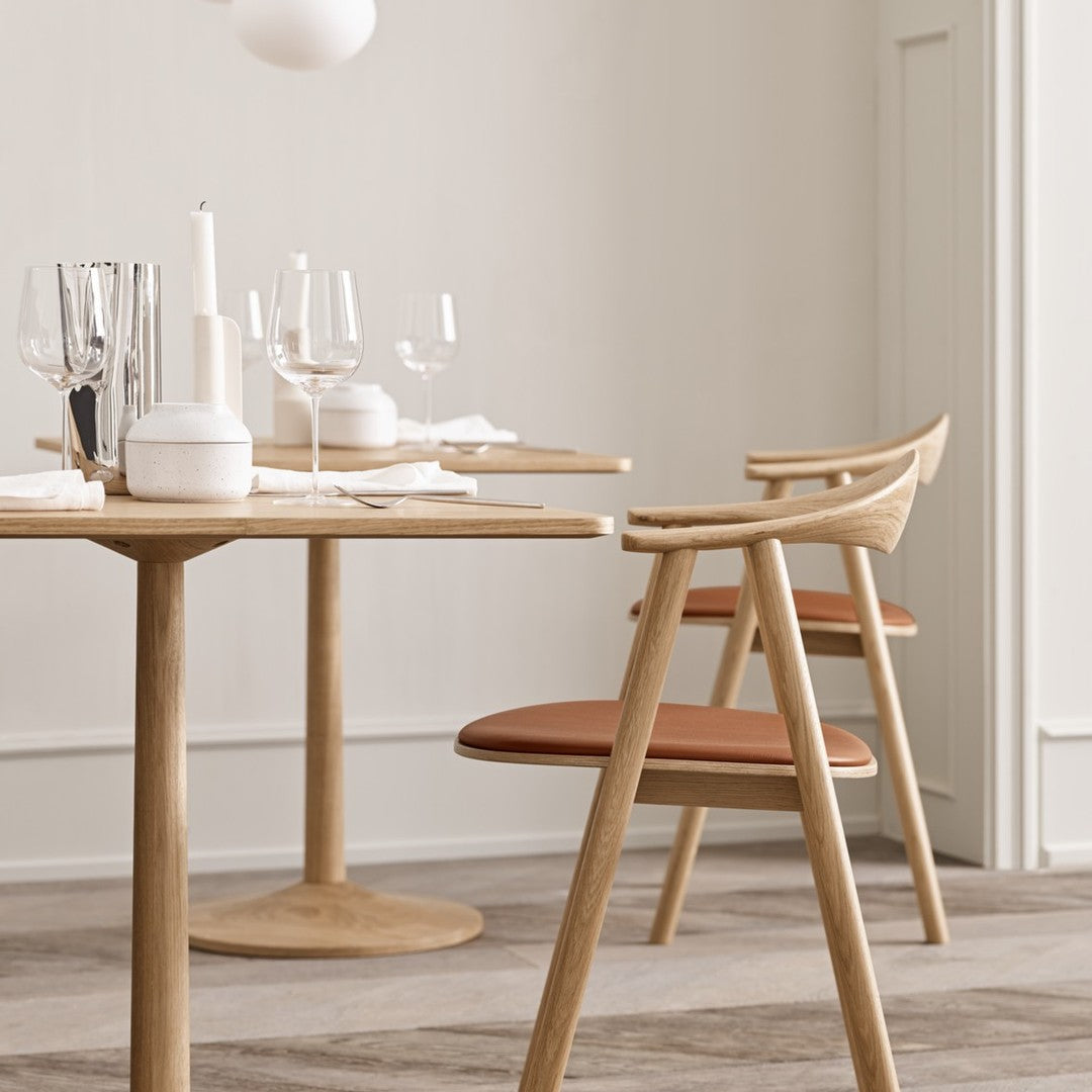 Light wood dining table with modern design and warm terracotta chair cushions, set against a neutral backdrop.