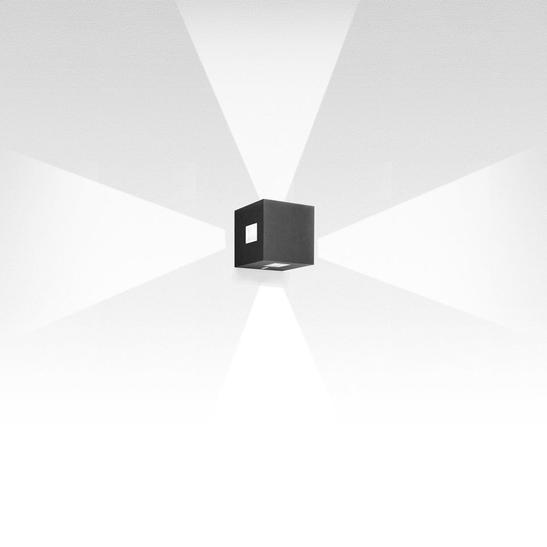 Black cube wall light with a sleek modern design, casting a soft white spotlight pattern on a light background.