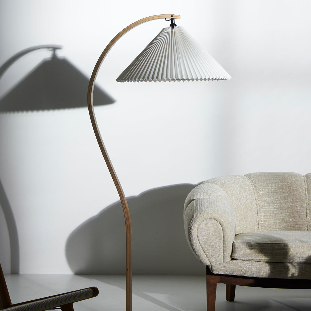 Elegant white pleated lampshade with natural wood base, casting soft shadows on a light backdrop. Ideal for modern decor.