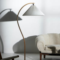Elegant white pleated lampshade with natural wood base, casting soft shadows on a light backdrop. Ideal for modern decor.