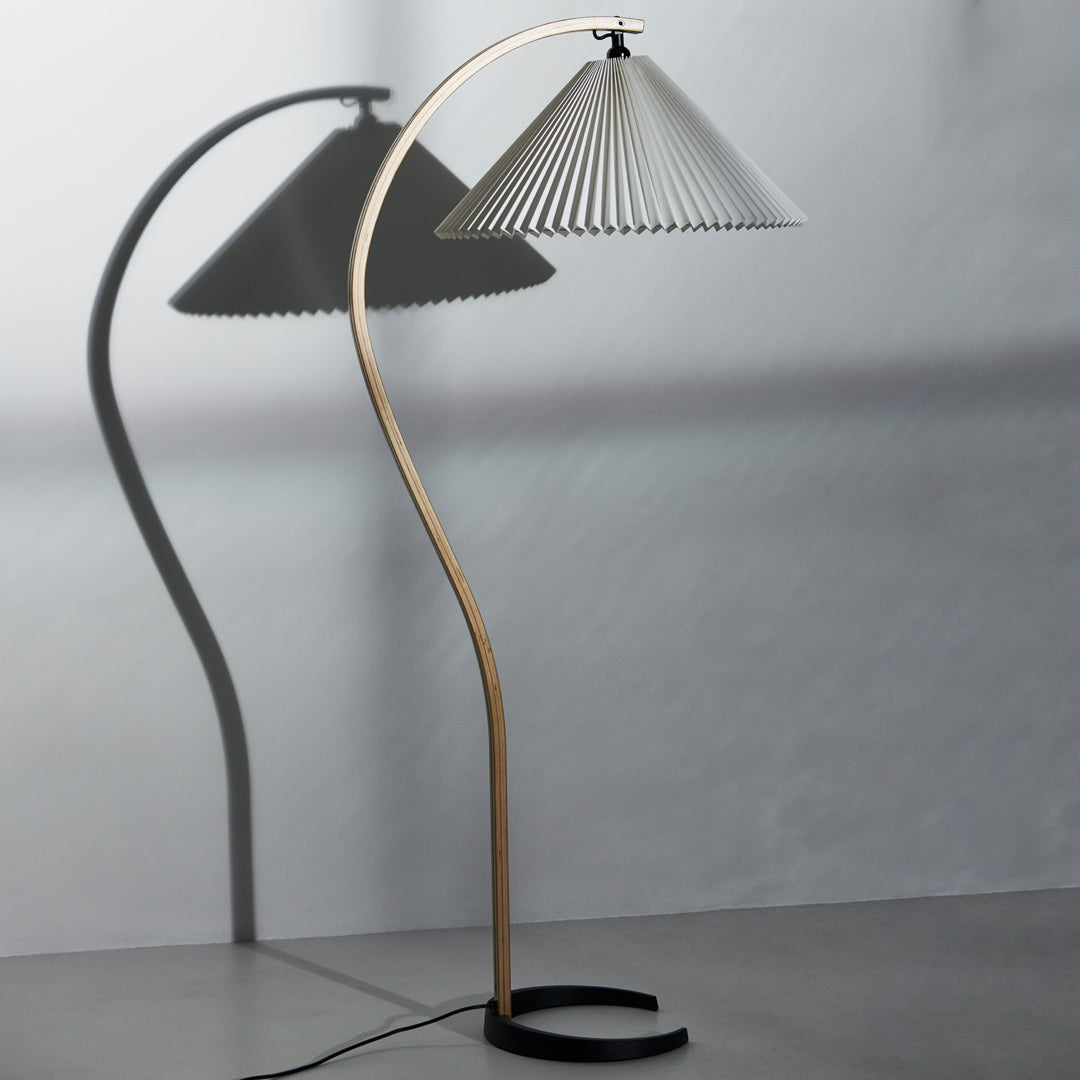 Modern floor lamp featuring a sleek gold base and a minimalist gray pleated shade casting soft shadows.
