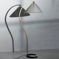 Modern floor lamp featuring a sleek gold base and a minimalist gray pleated shade casting soft shadows.