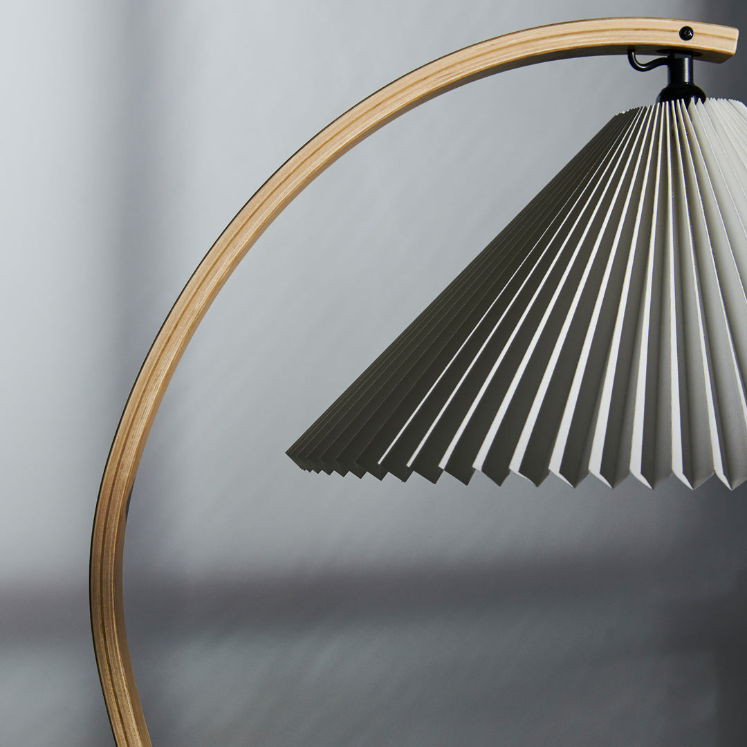 Modern floor lamp with a beige curved frame and a pleated gray shade, enhancing contemporary decor with sleek lines.