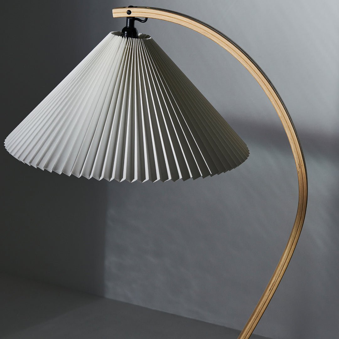 White pleated lamp shade with a wooden curved base, showcasing a modern, minimalist design.