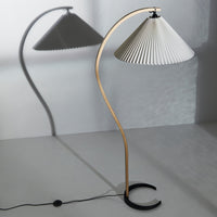 Elegant white pleated lamp shade with a light wood curved base and black circular stand, casting soft shadows.