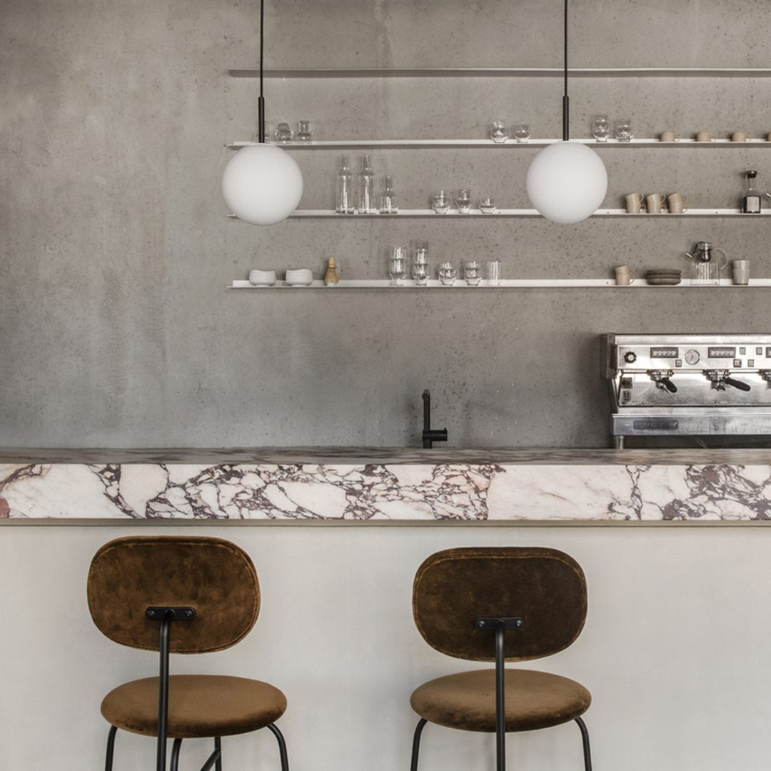 Modern bar with a textured gray wall, white globe pendant lights, and a marble countertop featuring soft pink and white patterns.
