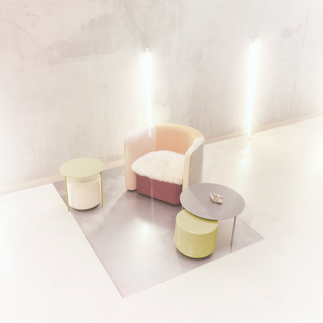 Pastel pink, cream, and light green armchair paired with yellow and white side tables on a minimalist silver mat.