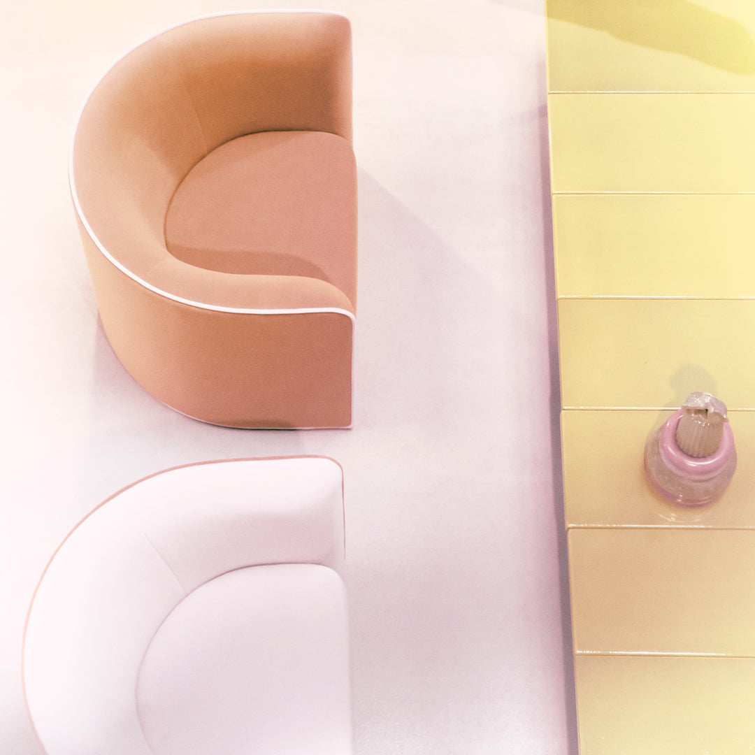 Two curved, pastel chairs in soft pink and peach tones on a light, yellow surface. Modern design with minimal patterns.