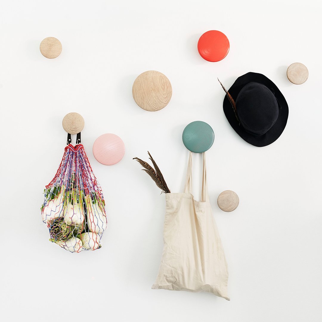 Colorful wall hooks in pastel pink, green, and orange, paired with a black hat and a textured mesh bag.
