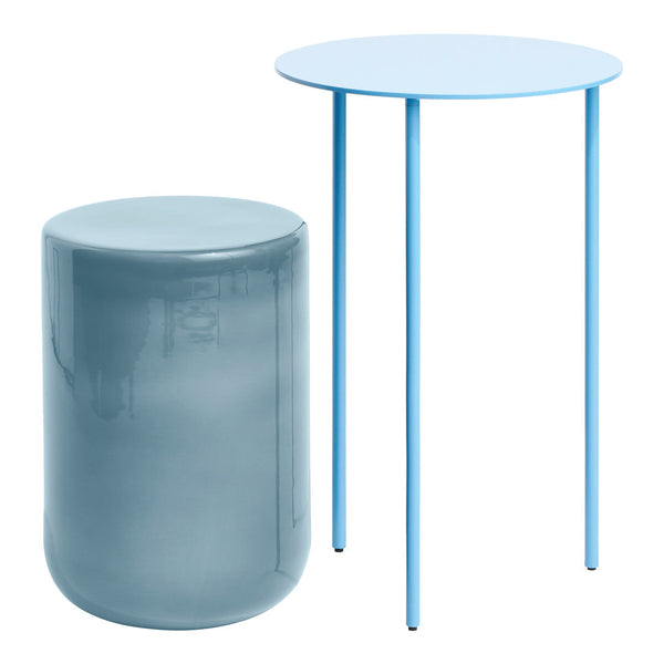 Light blue round side table with slender legs beside a cylindrical, glossy blue stool. Stylish modern design.
