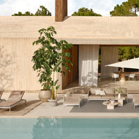Modern outdoor seating in neutral tones with a soft gray rug, surrounded by greenery and a tranquil blue pool.