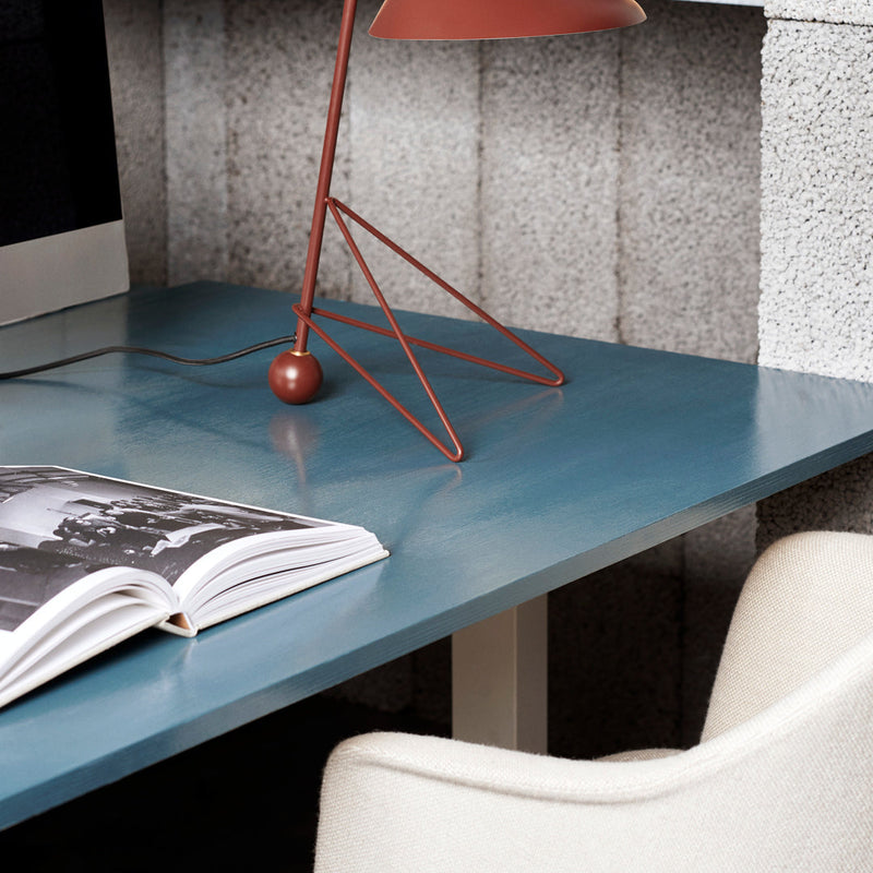 "Stylish blue desk surface with subtle glossy finish, accented by a modern copper lamp and a light beige chair."