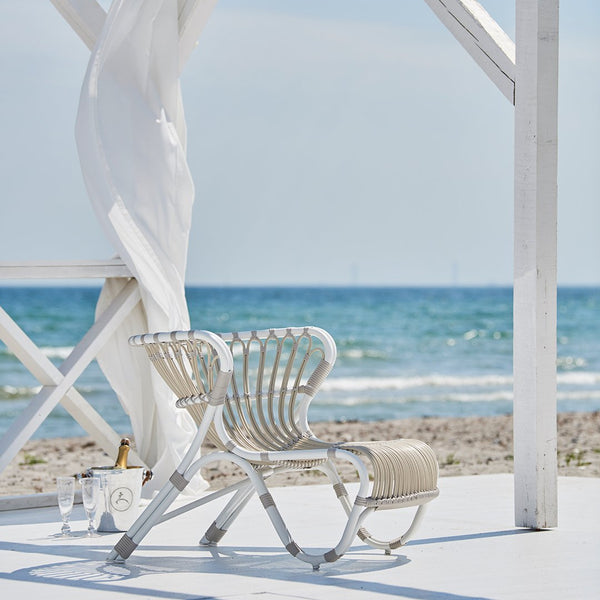 Stylish white beach chair with a striped cream and beige pattern, set against a serene ocean backdrop.