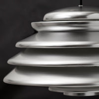 Silver layered pendant lamp with a sleek, modern design against a dark background.