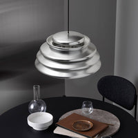 "Stylish silver layered pendant light on a modern black table, complemented by minimalist white and glass accessories."