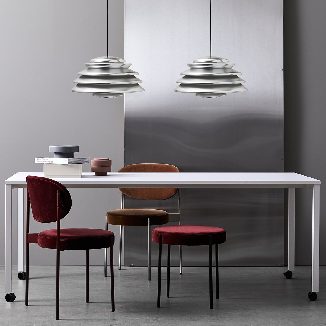 Stylish dining setup featuring a white table, red and brown patterned chairs, and sleek silver pendant lights.