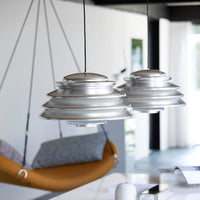 Metallic silver pendant lights with a layered design, complemented by a modern orange hanging chair and neutral surroundings.